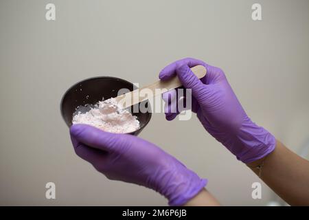 Il processo di preparazione della maschera di alginato rosa per il viso. Coppa nelle mani di un estetista. Foto Stock