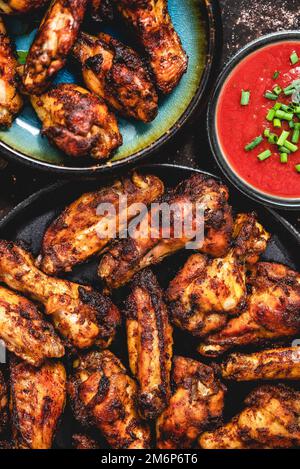 Ali di pollo grigliate su un piatto nero su uno sfondo rustico scuro Foto Stock