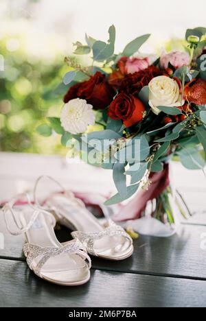 I sandali da sposa bianchi si trovano sul tavolo accanto al bouquet da sposa Foto Stock