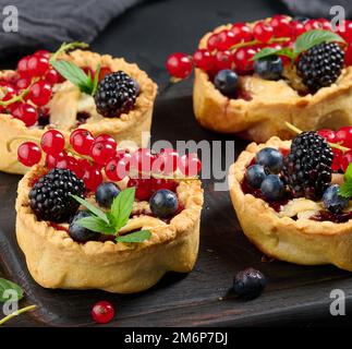 Crostata di frutta con ribes rosso cosparso di zucchero in polvere su un tavolo nero Foto Stock