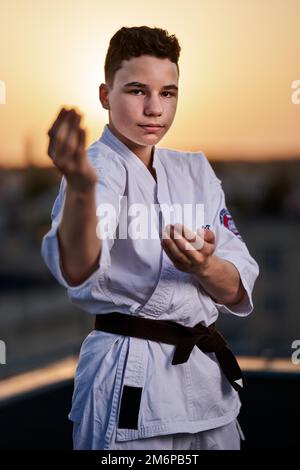 Giovane ragazzo praticante di karate in bianco kimono allenamento sul tetto al tramonto Foto Stock