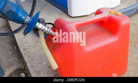 Rifornimento di benzina. Ugello della pompa di rifornimento e contenitore del carburante rosso presso la stazione di rifornimento carburante. Foto Stock