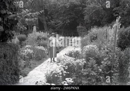 1950s, storico, una anziana signora visitatore nei giardini del cottage di Ann Hathaway, una fattoria in paglia a Shottery, Warwickshire, Inghilterra, Regno Unito, la casa d'infanzia della moglie del famoso drammaturgo inglese, William Shakespeare, che è nato nella vicina città di Stratford-upon-Avon. Foto Stock