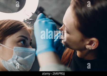 Giovane donna che fa piercing al salone di bellezza studio. Foto Stock