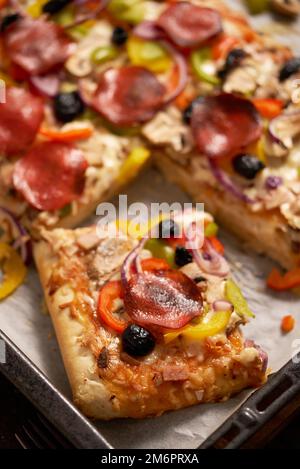 Un pezzo di pizza quadrata con pomodori peperoni al basilico e funghi su un vassoio di ferro Foto Stock