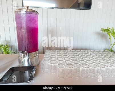 Bevanda a base di succo in un dispenser di bevande. Succo self-service in contenitore e bicchieri sul tavolo. Foto Stock