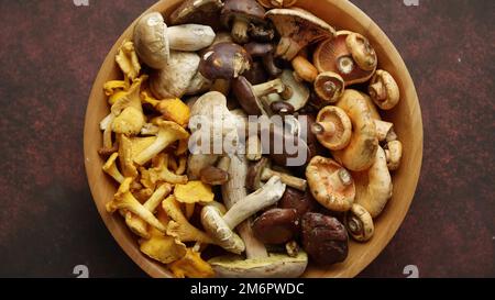 Vari tipi di funghi crudi assortiti messi in ciotola di legno Foto Stock