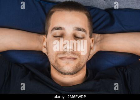 Vista dall'alto di un bel giovane che dorme comodamente sul letto nella sua camera da letto di notte. Bachelor camera da letto. Sonno profondo. Foto Stock