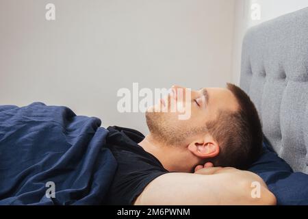 Vista dall'alto di un bel giovane che dorme comodamente sul letto di notte nella sua camera da letto. Dormire in diverse posizioni. Bachelor camera da letto. Sonno profondo. Foto Stock