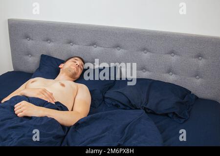 Bel giovane che dorme comodamente sul letto di notte nella sua camera da letto senza vestiti. Bachelor camera da letto. Sonno profondo. Foto Stock