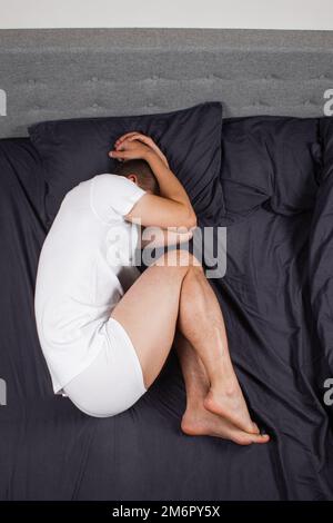 Bel giovane che dorme comodamente sul letto di notte nella sua camera da letto indossando pigiami. Bachelor camera da letto. Nella posizione fetale. Foto Stock