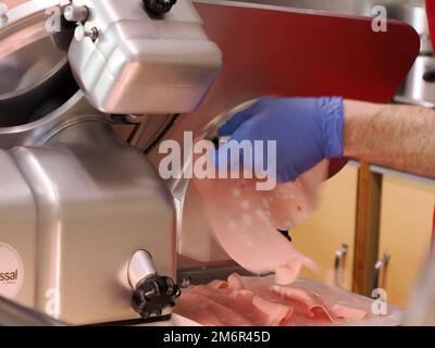 Diverse salsicce tradizionali italiane nel negozio tagliando fette di mortadella Foto Stock