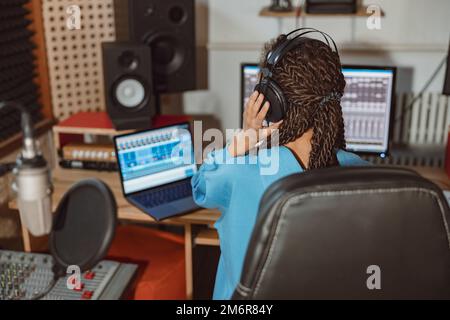 Vista posteriore di un presentatore radiofonico, di una donna ancora, di un tecnico del suono che indossa le cuffie e lavora in uno studio di radiodiffusione Foto Stock