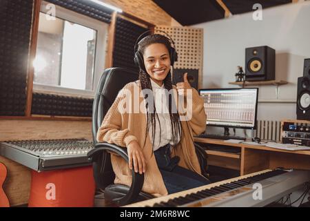 Splendida donna africana elegante ingegnere audio, musicista e produttore mostrando pollice in su lavorando in studio di registrazione musicale Foto Stock