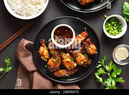 Ali appiccicose di pollo al miele e alla soia sul piatto su sfondo di pietra scura. Vista dall'alto, disposizione piatta, primo piano Foto Stock