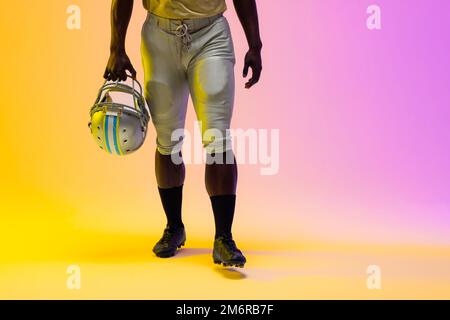 Sezione centrale del giocatore di calcio afro-americano maschile con illuminazione viola e gialla al neon Foto Stock