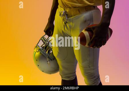 Sezione centrale del giocatore di calcio afro-americano maschile con illuminazione viola e gialla al neon Foto Stock