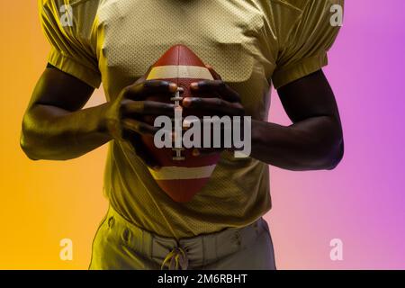 Sezione centrale del giocatore di calcio afro-americano maschile con illuminazione viola e gialla al neon Foto Stock