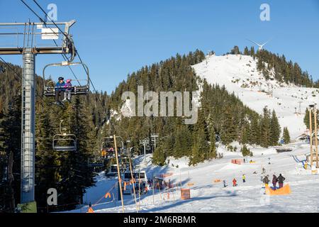 Vancouver, Canada - 16 dicembre 2022: Vista della seggiovia con le persone al Grouse Mountain Ski Resort con The Eye of the Wind sullo sfondo Foto Stock