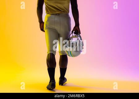 Sezione centrale del giocatore di calcio afro-americano maschile con illuminazione viola e gialla al neon Foto Stock