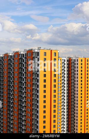 Nuovi edifici residenziali con rivestimento arancione e giallo sullo sfondo del cielo con nuvole bianche, scatto verticale. Sviluppo della casa Foto Stock