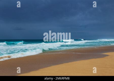 Onde turchesi che si lavano su una spiaggia di sabbia sotto un cielo coperto Foto Stock