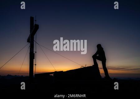 Gli alpinisti alla croce sommitale del Namloser Wetterspitze al tramonto con Lechtaler Alpen, Namlos, Reutte, Lechtal, Ausserfern, Tirolo, Austria Foto Stock