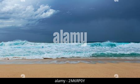 Onde turchesi che si lavano su una spiaggia di sabbia sotto un cielo coperto Foto Stock