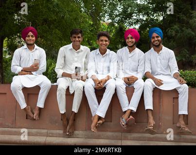 Giovani uomini in tute bianche e a piedi nudi nel Parco di Jallianwalla Bagh, Delhi, India Foto Stock