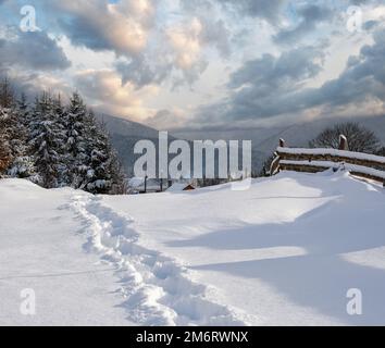 Colline di campagna, boschi e terreni agricoli in inverno remoto villaggio di montagna alpina. Sentiero fresco trodden escursionismo. Foto Stock