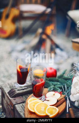 Due bicchieri di bibita di vino caldo tritato con agrumi, mele, bastoncini di cannella, chiodi di garofano e anice su fondo di tavola di legno Foto Stock