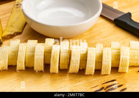 Vista in primo piano della banana organica matura tagliata a fette sbucciata sul tagliere. Foto Stock