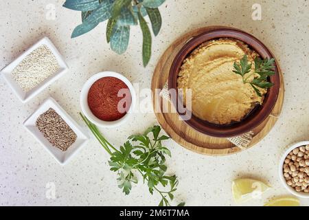 Hummus nella ciotola, prezzemolo, limone, paprika, semi di cumino romano, ceci, ingredienti per sesamo. Vegetariano sano naturale rustico cibo Foto Stock