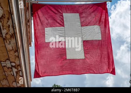 Bandiera svizzera. Bandiera svizzera sospesa sul tetto contro il cielo blu. Una bandiera rossa quadrata con una croce bianca al centro. Oggetti. Foto Stock