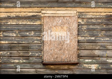 Una vecchia finestra di legno si è imbarcata con legno compensato su una parete di legno Foto Stock