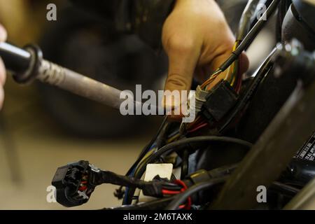 Un elettricista sta saldando i fili elettrici alle apparecchiature elettriche di una motocicletta. Primo piano. Concetto di trasporto Foto Stock