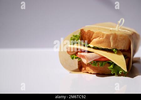 Panino di formaggio e prosciutto avvolto in carta su sfondo bianco con spazio copia Foto Stock