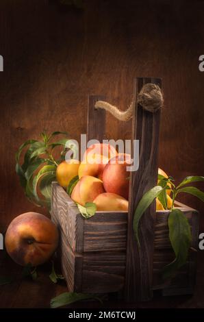 Nettarine in una scatola di legno su uno sfondo di legno scuro in uno stile rustico Foto Stock