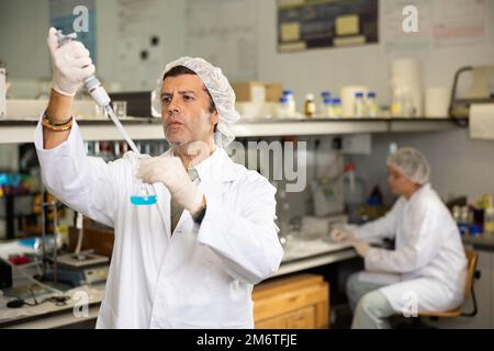 Biologo latino-uomo concentrato con pipetta meccanica da laboratorio per la miscelazione di prodotti chimici in laboratori moderni Foto Stock