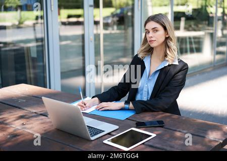 Donna d'affari di successo che lavora all'aperto. Donna aziendale seduta su panca con computer portatile, scrivere, prendere appunti durante il lavoro meeti Foto Stock
