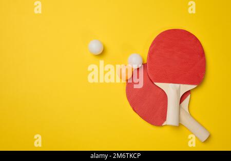 Coppia di racchette da tennis in legno per ping pong e palle di plastica su sfondo giallo Foto Stock