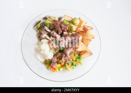 Pasto cucinato su un piatto di vetro un pasto di carne e verdure di maiale e crackling Cauliflower Brussel germogli di Broccoli funghi e patate arrosto Foto Stock