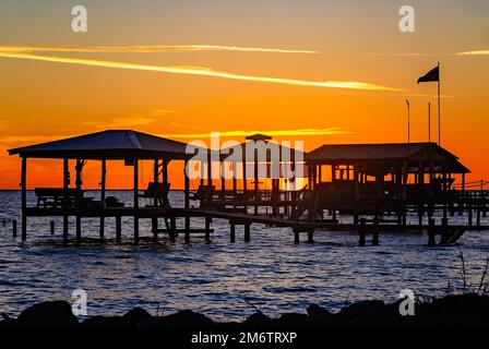 Il sole tramonta dietro le banchine e i moli per la pesca, il 4 gennaio 2023, a Coden, Alabama. Foto Stock