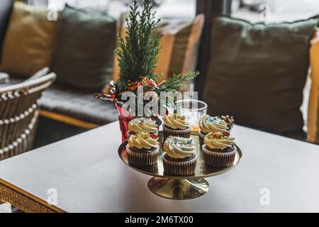 Caffè interno con prodotti da forno. Stand d'oro posto sul tavolo con adorabili cupcake con gelato alla vaniglia e spruzzate colorate. Natale. Foto di alta qualità Foto Stock