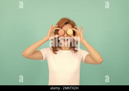 divertente ragazza tenere dolce macaron biscotto francese su sfondo blu Foto Stock