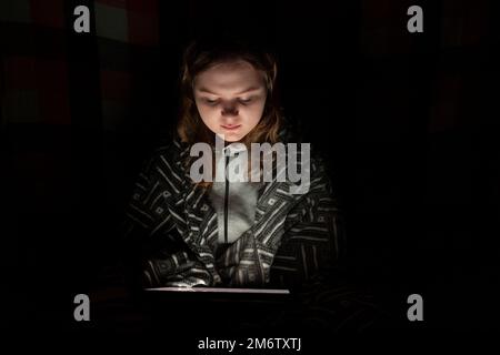 Una ragazza usa un tablet pc in una stanza buia. Blackout. Crisi energetica. Distruzione delle infrastrutture. Concetto di interruzione dell'alimentazione Foto Stock