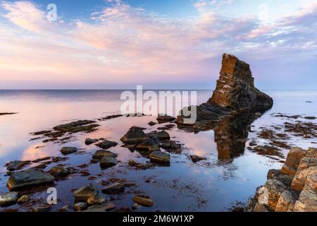 Tramonto colorato sulla costa del Mar Nero della Bulgaria, con uno stack di mare e rocce in acque calme Foto Stock