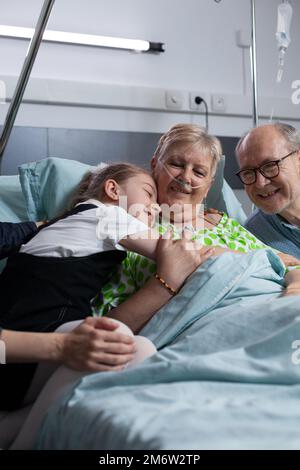 Donna sotto controllo medico in pazienti geriatrici clinica coccole nipote giovane in camera da letto. Nonno, bambina che visita la signora anziana malata nella zona di riposo dell'ospedale. Foto Stock