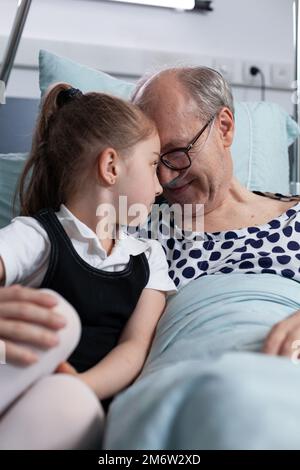 Nonno ricoverato sorpreso, felice da poco nonna visita inaspettata in ospedale sala di osservazione. Ragazza che mostra affetto fisico, abbracciando l'uomo anziano malato in clinica geriatrica. Foto Stock