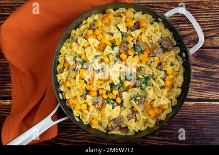 Pasta cremosa di zucca arrosto con salsiccia e spinaci in una padella: Padella piena di cibi dolci fatti con zucca invernale in salsa di panna Foto Stock